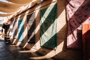 Textiles hang on a brick wall with striped shadows.