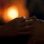 Hands massaging a person's face in a dimly lit room with warm bokeh