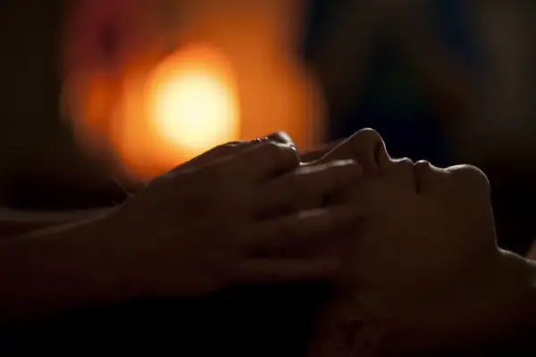 Hands massaging a person's face in a dimly lit room with warm bokeh